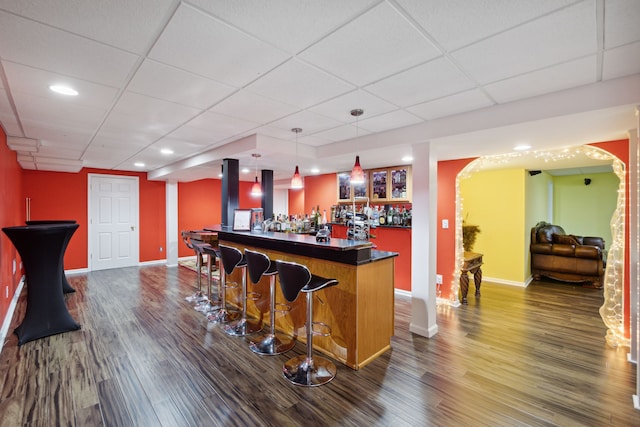 bar with dark wood finished floors, a dry bar, decorative light fixtures, and a drop ceiling