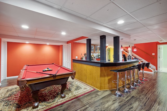 recreation room with a dry bar, wood finished floors, baseboards, and a drop ceiling