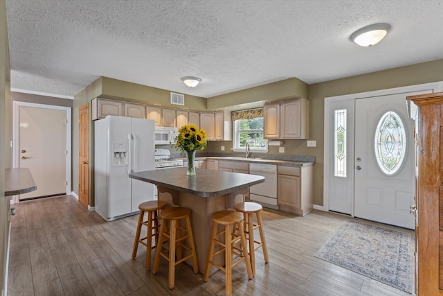 kitchen with visible vents, a kitchen island, light wood-type flooring, a kitchen bar, and white appliances