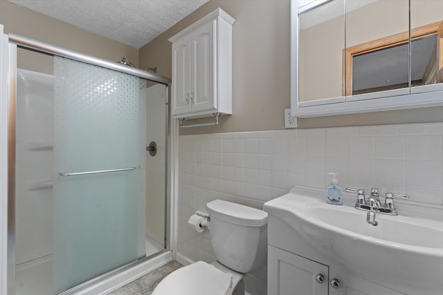 bathroom with a shower stall, toilet, vanity, a textured ceiling, and tile walls