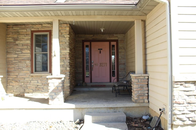 view of exterior entry featuring stone siding, roof with shingles, and a porch