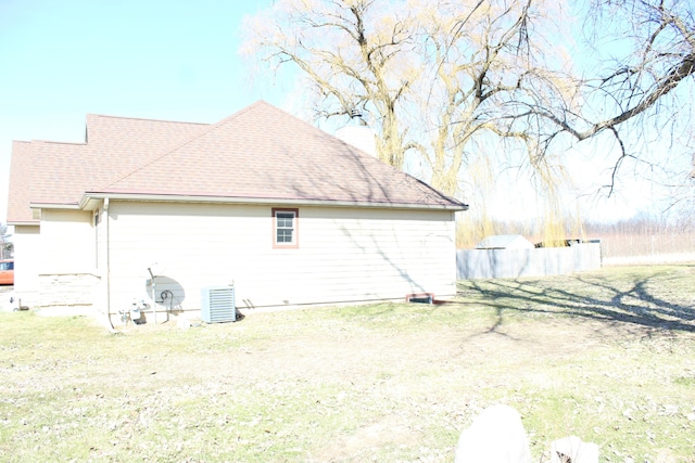 view of side of home featuring a lawn, central AC, and a shingled roof