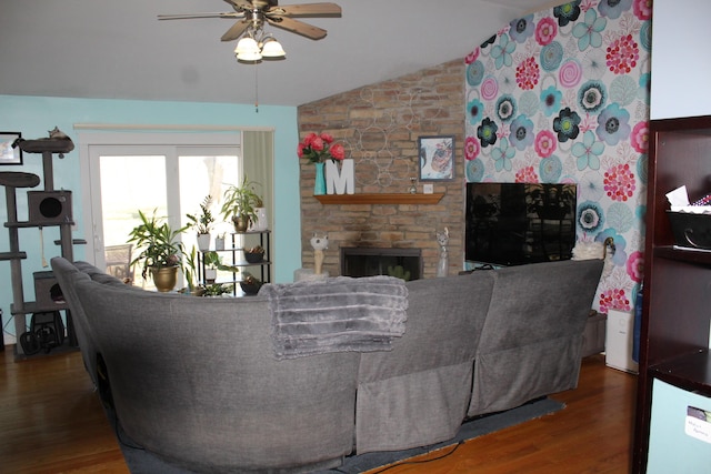 living room with a stone fireplace, vaulted ceiling, wood finished floors, and ceiling fan