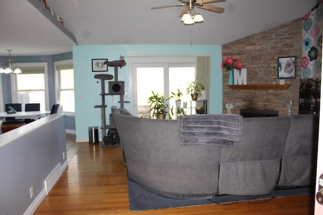 living area with visible vents, vaulted ceiling, a stone fireplace, wood finished floors, and a ceiling fan