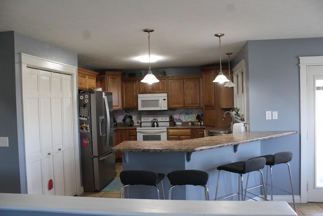 kitchen with brown cabinets, a kitchen breakfast bar, a peninsula, white appliances, and a sink