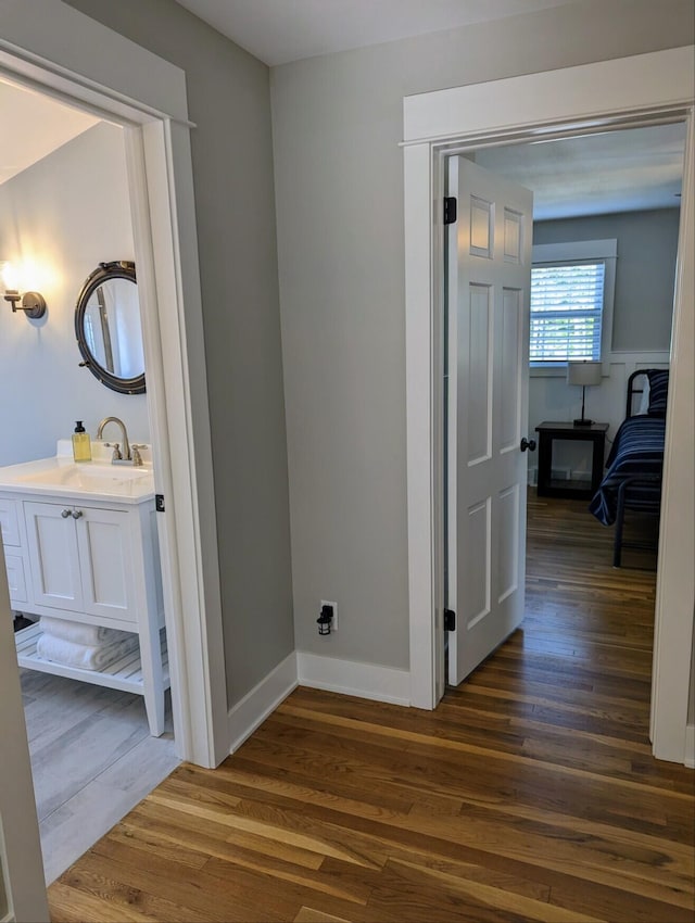 hall featuring a sink, baseboards, and dark wood-style flooring