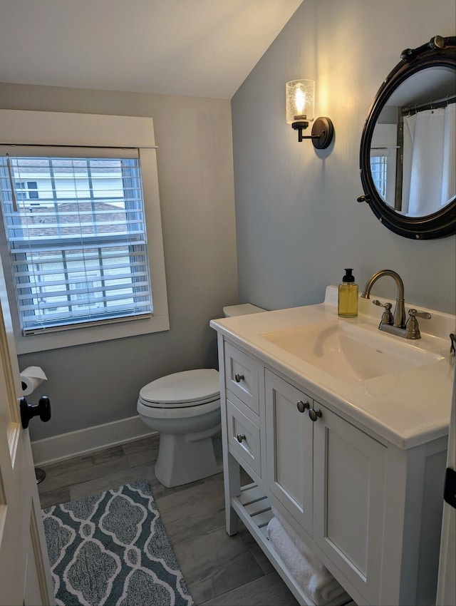 bathroom with toilet, wood finished floors, baseboards, vanity, and vaulted ceiling