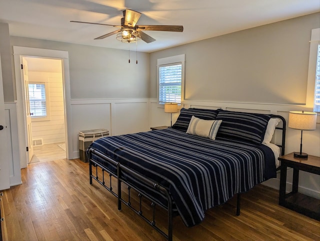 bedroom featuring ceiling fan, wood finished floors, visible vents, and wainscoting