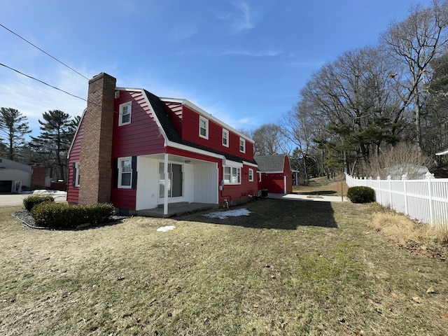 rear view of house with a gambrel roof, a chimney, a yard, and fence