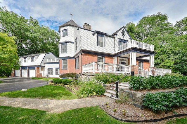 view of front of home with a front yard, a balcony, driveway, a chimney, and brick siding