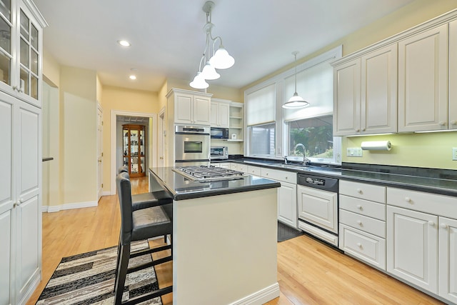 kitchen with paneled dishwasher, a sink, stainless steel gas stovetop, dark countertops, and light wood-type flooring