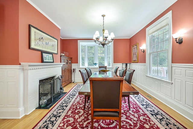 dining space with light wood finished floors, visible vents, crown molding, a chandelier, and a wainscoted wall