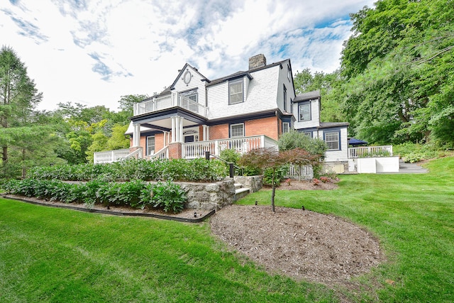 view of front of property with a front yard, brick siding, a chimney, and a balcony