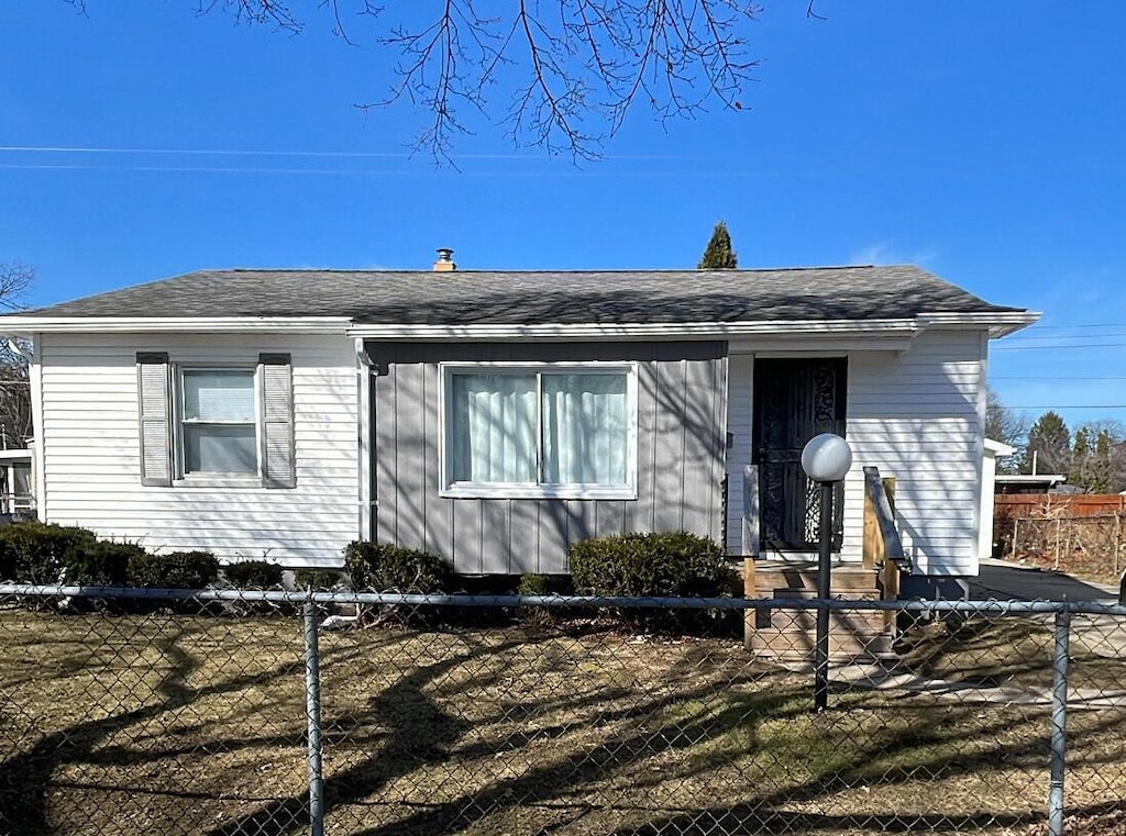 view of front of property with entry steps, a fenced front yard, and a shingled roof