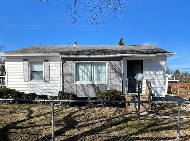 view of front of property with entry steps, a fenced front yard, and a shingled roof