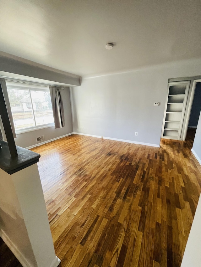 unfurnished living room featuring visible vents, baseboards, and wood finished floors