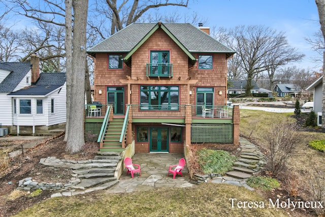 view of front facade featuring a patio, stairway, french doors, a balcony, and a chimney