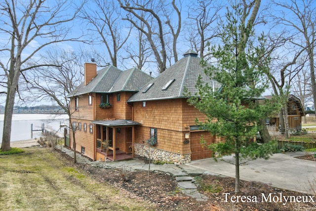 view of front of home featuring a water view, stone siding, and a chimney