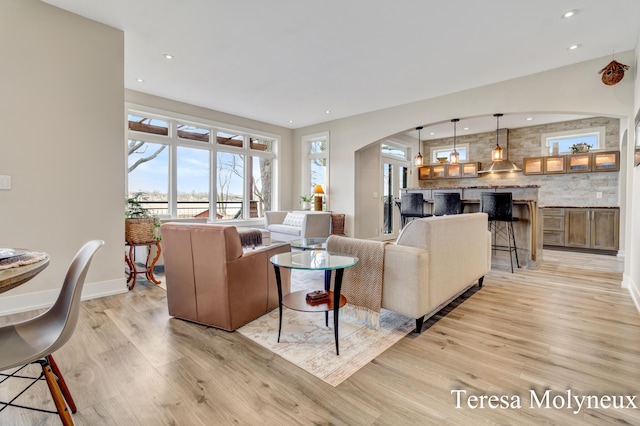 living area with recessed lighting, light wood-style floors, arched walkways, and baseboards