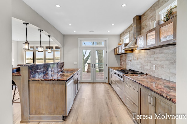 kitchen with light wood finished floors, stainless steel gas cooktop, a breakfast bar, dark stone counters, and a sink