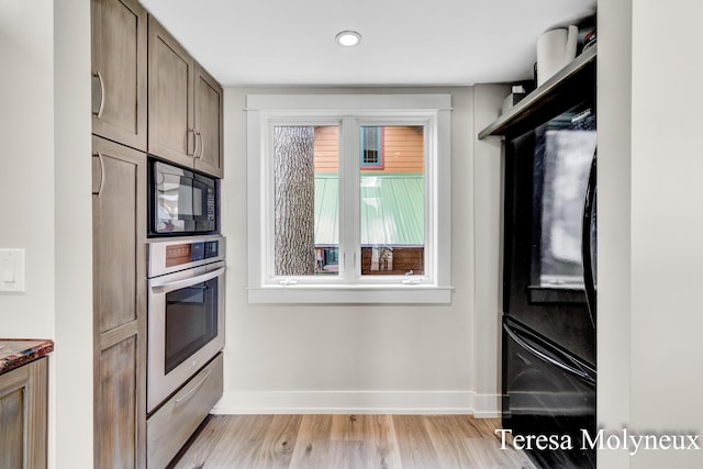 kitchen with dark stone countertops, baseboards, light wood finished floors, black microwave, and stainless steel oven