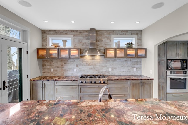 kitchen with oven, a warming drawer, dark stone counters, wall chimney exhaust hood, and black microwave