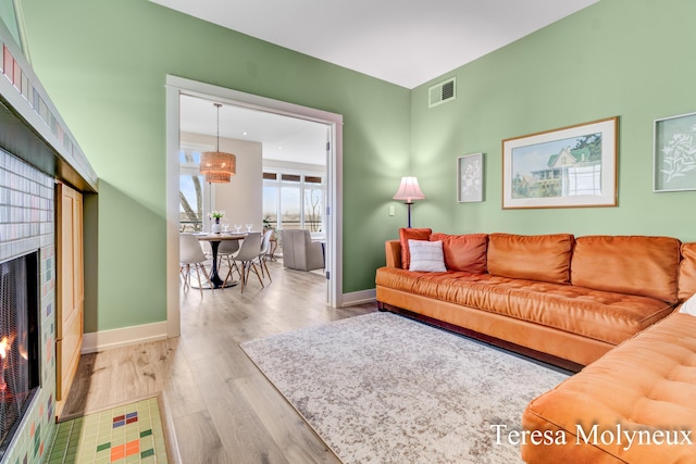 living room with a lit fireplace, visible vents, baseboards, and wood finished floors