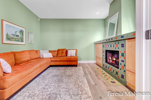 living area featuring a tiled fireplace, recessed lighting, baseboards, and wood finished floors