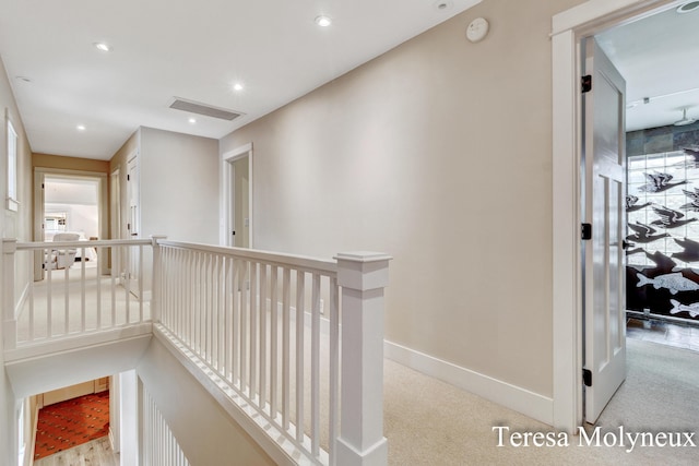 hallway featuring an upstairs landing, visible vents, carpet floors, and baseboards