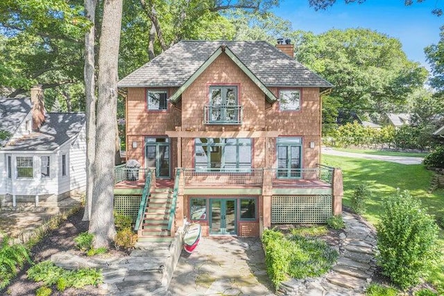 view of front facade with a chimney, a front lawn, french doors, a wooden deck, and stairs