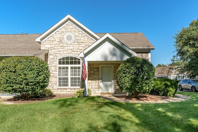 view of front of house with a front yard, stone siding, and roof with shingles