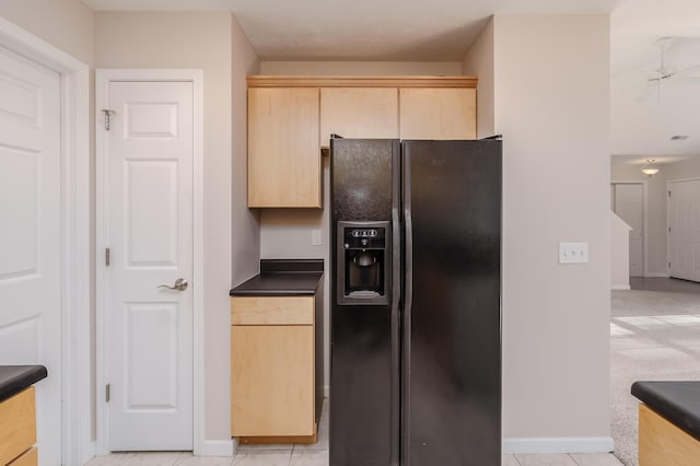 kitchen featuring dark countertops, black fridge with ice dispenser, light brown cabinets, and baseboards