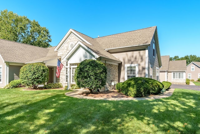 view of front of property with stone siding, roof with shingles, and a front lawn