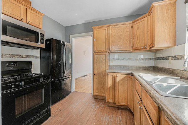 kitchen with light wood-style flooring, a sink, black appliances, light countertops, and tasteful backsplash