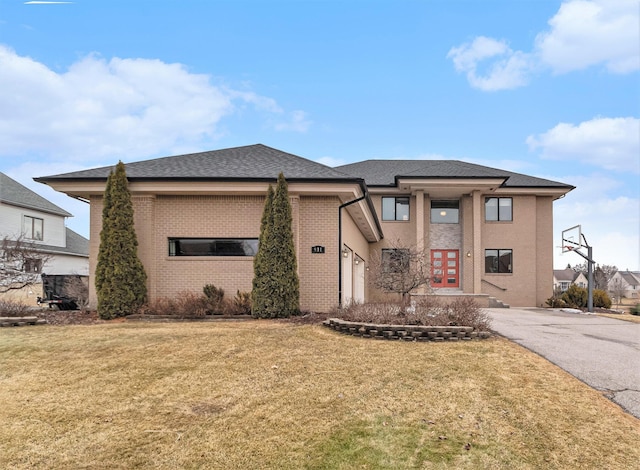 prairie-style home featuring brick siding, a shingled roof, aphalt driveway, a front yard, and french doors