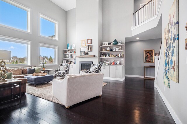 living area featuring a glass covered fireplace, a healthy amount of sunlight, dark wood-type flooring, and a towering ceiling