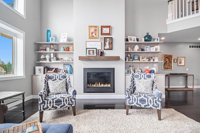 living room with a glass covered fireplace, baseboards, wood finished floors, and visible vents
