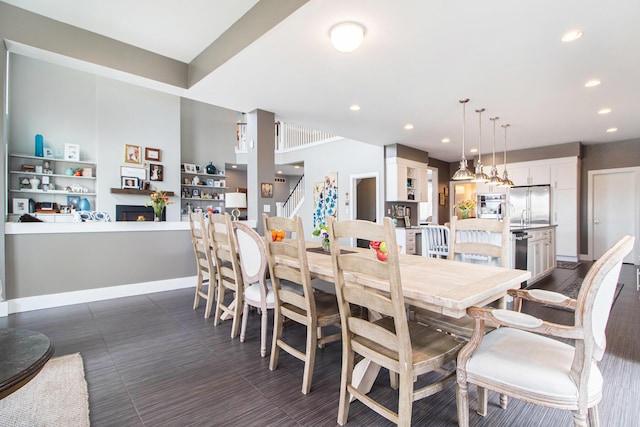 dining room featuring stairway, baseboards, recessed lighting, and a warm lit fireplace
