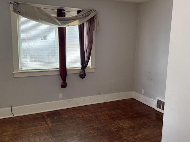 empty room with wood finished floors, visible vents, and baseboards