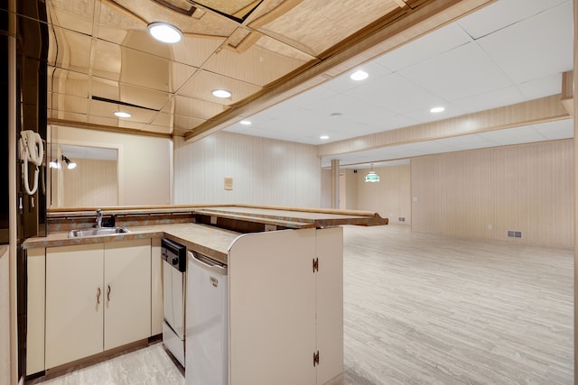 kitchen featuring a peninsula, light wood-type flooring, dishwasher, and a sink