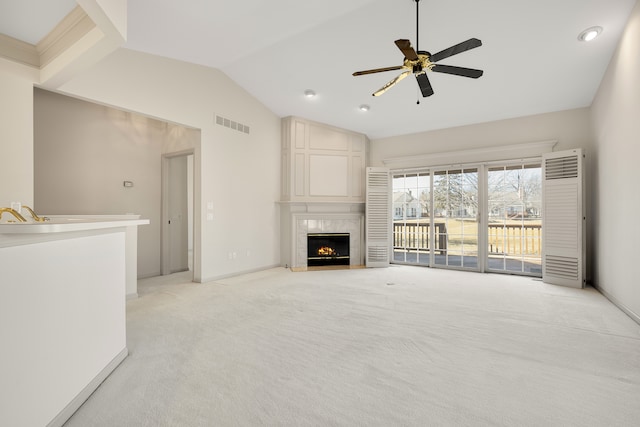 unfurnished living room featuring a ceiling fan, visible vents, a premium fireplace, vaulted ceiling, and light colored carpet