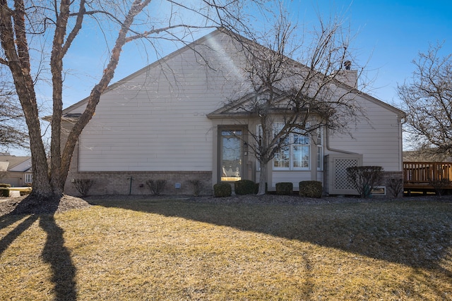 rear view of house with brick siding, a deck, a chimney, and a yard