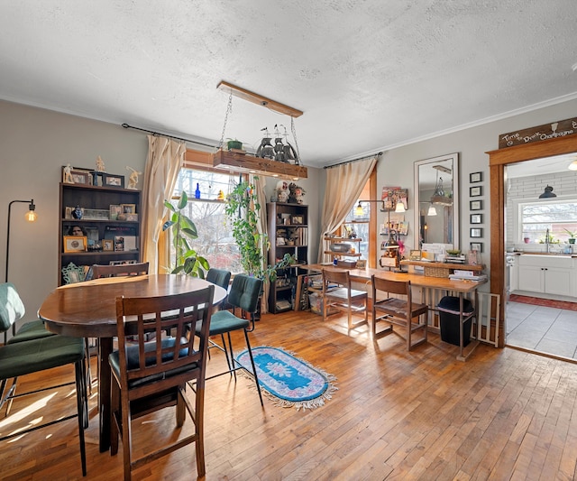 dining room featuring a healthy amount of sunlight, a textured ceiling, ornamental molding, and hardwood / wood-style floors