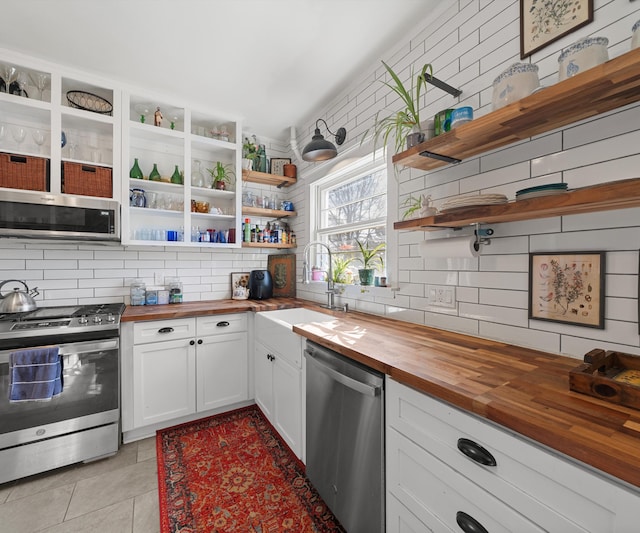 kitchen featuring open shelves, a sink, stainless steel appliances, wood counters, and tasteful backsplash