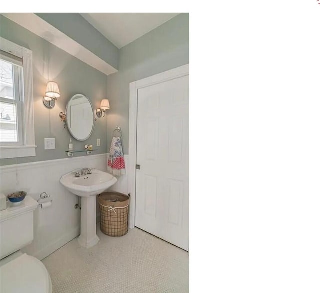 bathroom with toilet, a wainscoted wall, and a sink