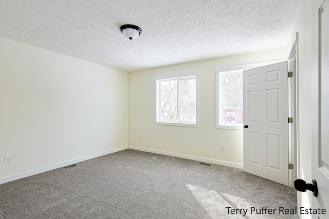 unfurnished room with visible vents, a textured ceiling, baseboards, and carpet