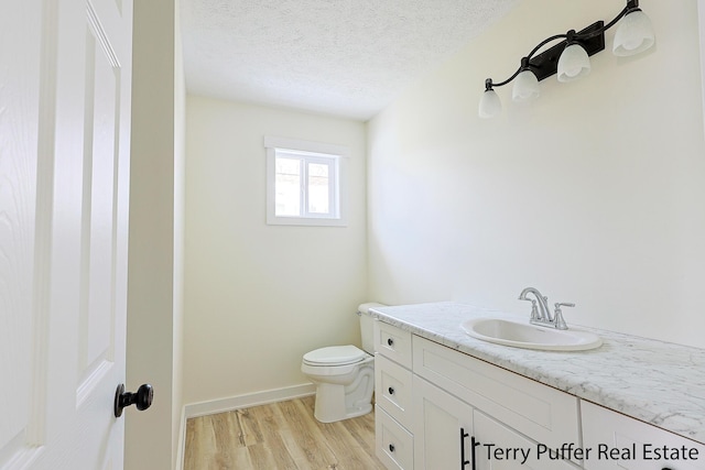 bathroom featuring toilet, a textured ceiling, wood finished floors, baseboards, and vanity