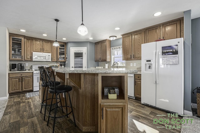 kitchen with a kitchen bar, dark wood-type flooring, a center island, white appliances, and glass insert cabinets