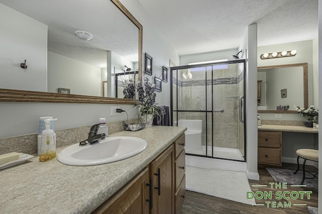 full bathroom featuring vanity, wood finished floors, a stall shower, and a textured ceiling