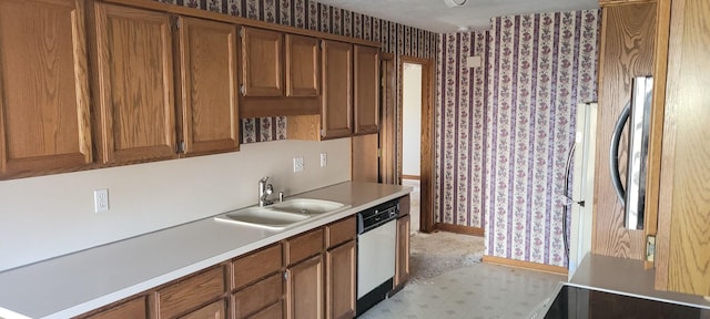 kitchen featuring wallpapered walls, light countertops, brown cabinets, white dishwasher, and a sink